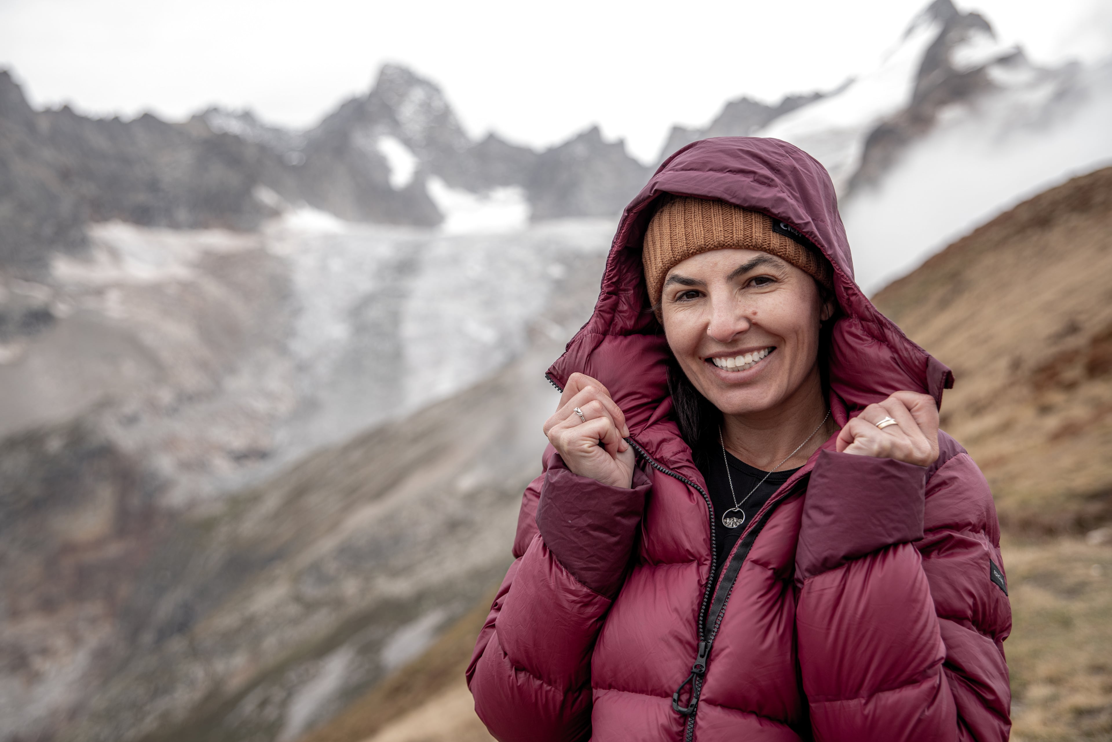 Mulher sorrindo diante de uma geleira, usando colar e anéis da Feito na Montanha